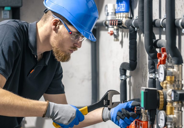 A man installs a heating system in a house and checks the pipes with a wrench. Adjusting heating valves in a residential building. A plumbing and heating technician works.