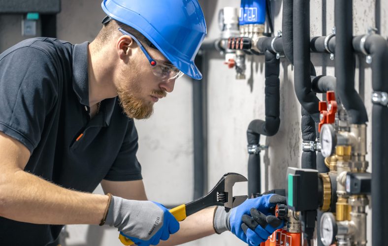 A man installs a heating system in a house and checks the pipes with a wrench. Adjusting heating valves in a residential building. A plumbing and heating technician works.